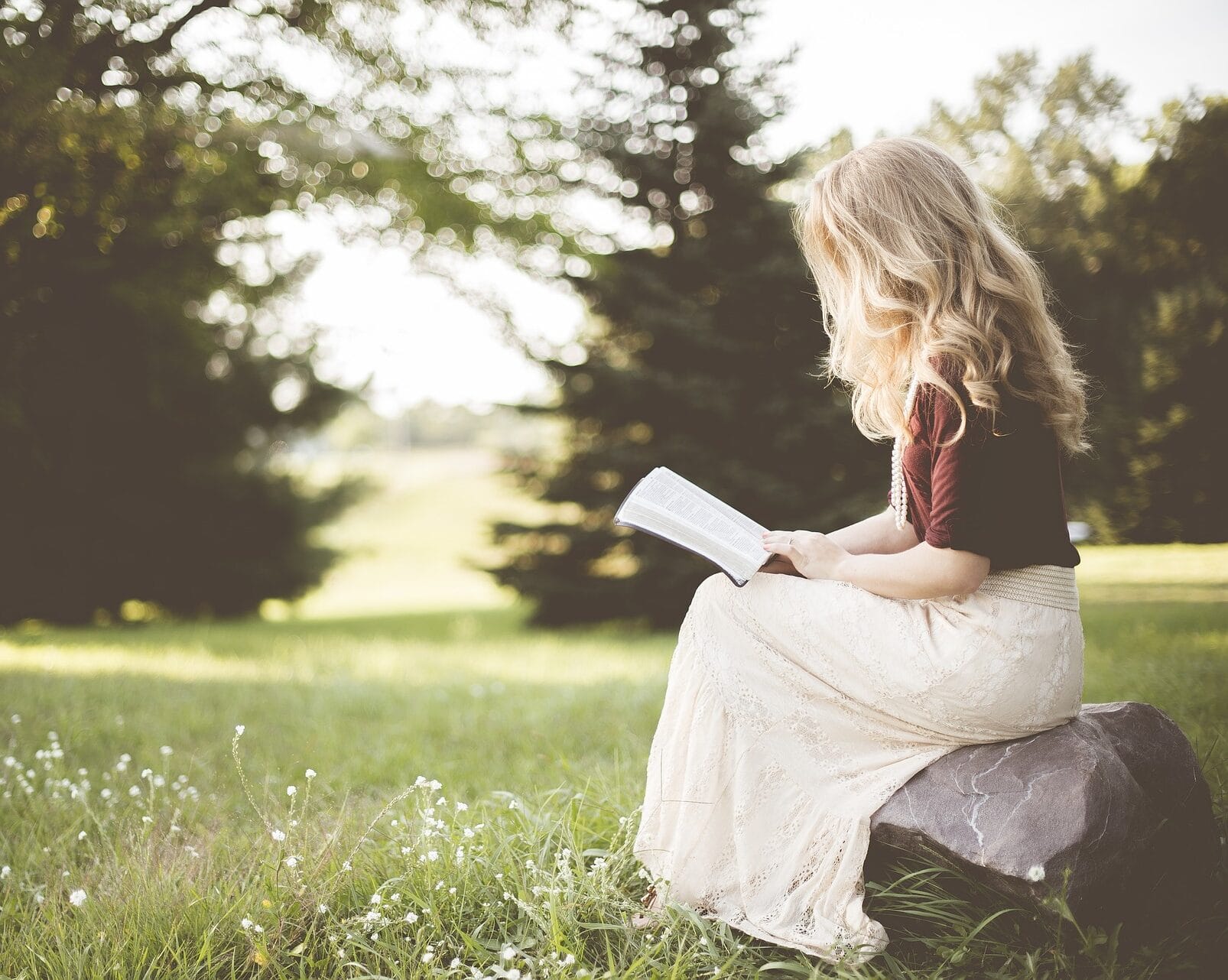 nainen istuu luonnossa ja lukee kirjaa